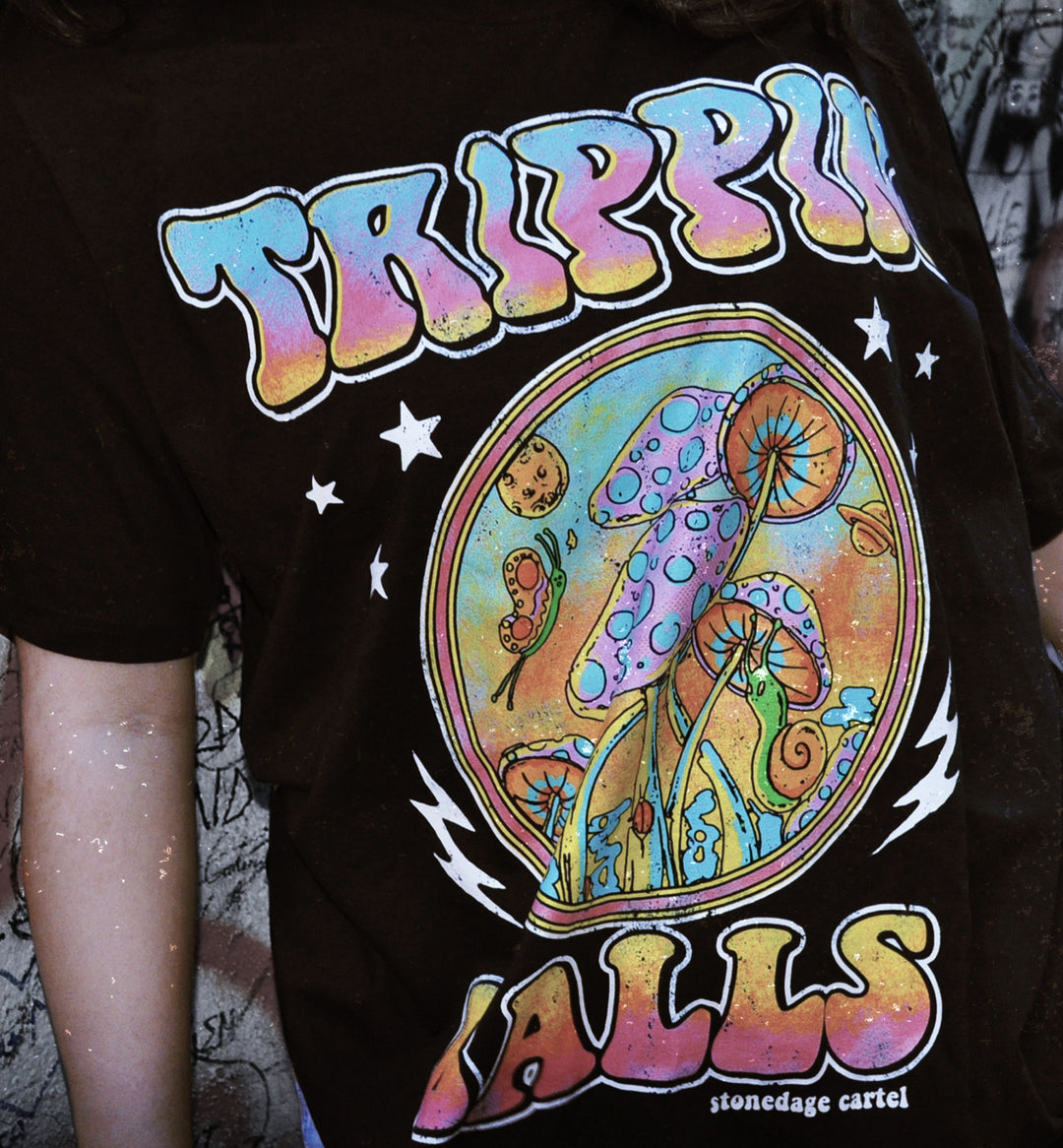 A close-up of a person wearing a black graphic t-shirt featuring a colorful psychedelic mushroom design with the text 'TRIPPIAN BALLS' and 'stoneage cartel' printed below.